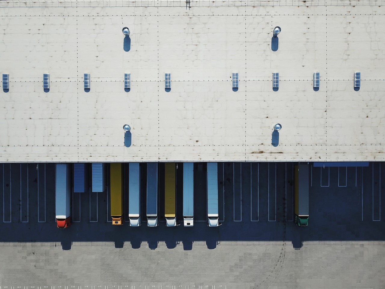 1292715506 Aerial view of goods warehouse. Logistics center in industrial city zone from above. Aerial view of trucks loading at logistic center